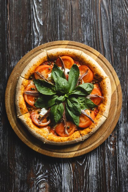 Appetizing pizza with tomatoes anchovies and basil on a wooden background