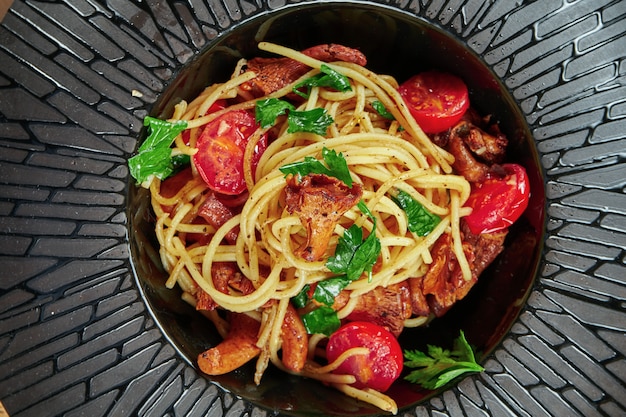 숲 버섯 (chanterelles) 체리 토마토와 나무 테이블에 검은 접시에 ruccola와 수 제 이탈리아 파스타 (스파게티)의 식욕을 돋 우는 부분. 식당 테이블 설정