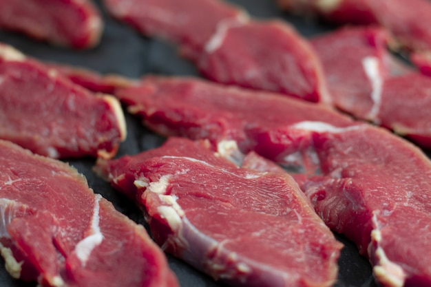 Appetizing red fresh veal, sliced into raw thin beef steaks, laid out on a black stone slate. 