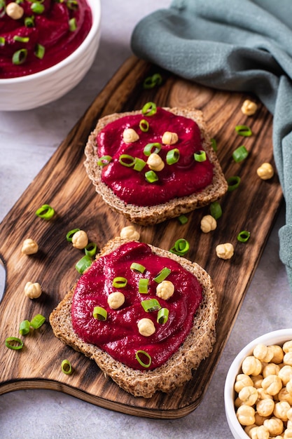 Appetizing rye bread bruschettas with beetroot hummus and chives on a cutting board vertical view