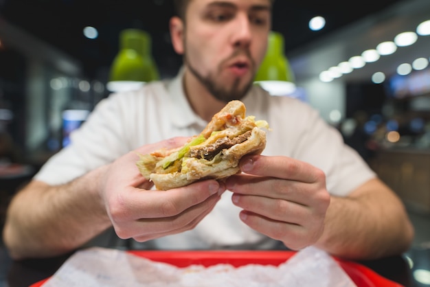 Un appetitoso panino nelle mani di un uomo. un uomo mangia un panino in un fast-food. concentrati sul panino