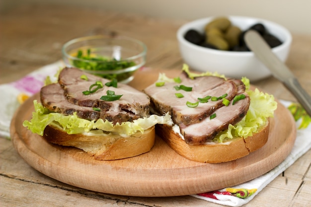 Appetizing sandwiches with meat, lettuce and sauce served with olives. Rustic style.