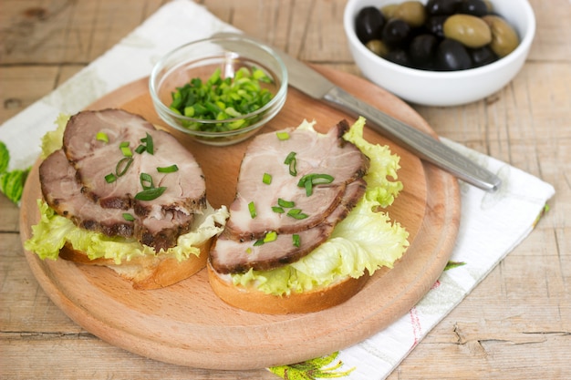 Аппетитные бутерброды с мясом, листьями салата и соусом подаются с оливками. Деревенский стиль