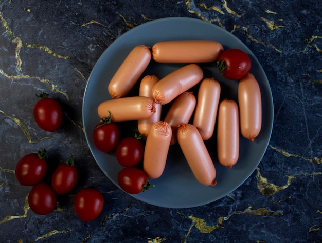 Photo appetizing sausages on a grey plate on a dark marble background close up