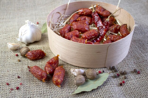 Appetizing sausages with garlic and spices in wood basket on rough linen background flatlay close up