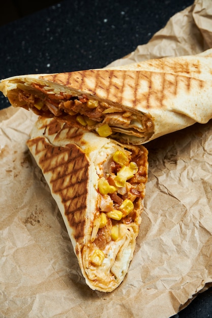 검은 표면에 공예 종이에 얇은 피타 빵에 고기, 샐러드 및 수제 소스로 식욕을 돋우는 shawarma 롤. 동부 요리. 구운 고기와 케밥 슬라이스.