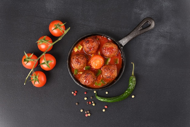 Appetizing stewed meatballs in tomato sauce in a pan on a dark background.