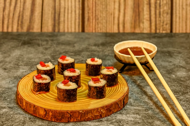 Appetizing sushi rolls with salmon rice and red pepper on a wooden plate