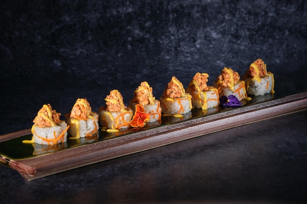 Appetizing sushi topped with salmon and fresh sauce served on wooden plate on marble table in restaurant against black background