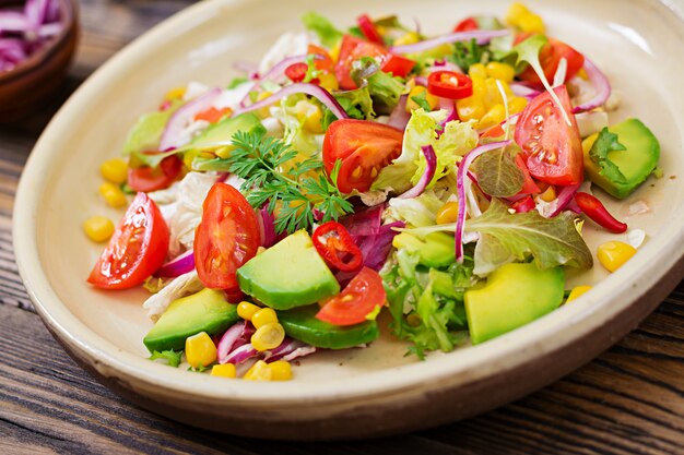 Appetizing vegan salad from tomatoes, avocado, corn, red onion and lettuce leaves. Tasty vegan food. Healthy vegan food. Vegetarian salad.