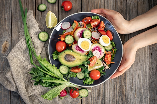 Appetizing vegetable salad with eggs avocado on a wooden background