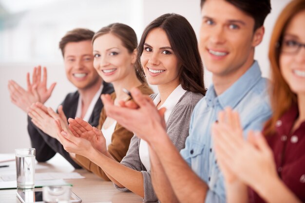 Applaudisseren voor jou. groep jongeren die samen aan tafel zitten en voor je applaudisseren