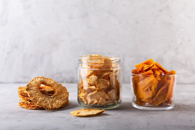 Apple, ananas en mango chips in een pot en stukjes van dit fruit op een tafel