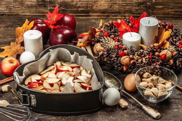 Apple charlotte is ready to bake. Kitchen utensil, set of ingredients, seasonal decor. Cooking sweet pastries with spices. Old wooden background, copy space