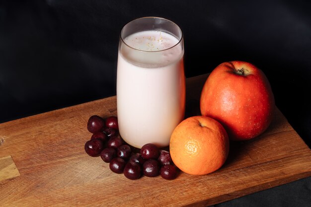 Apple cherry citrus smoothie op een houten bord met fruit op een zwarte ondergrond