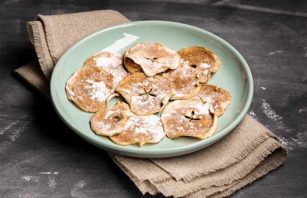 Apple chips sprinkled with powdered sugar and cinnamon on green plate on burlap 