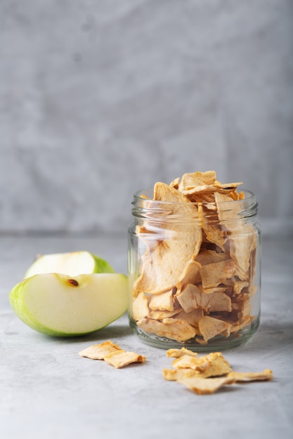 Apple chips in a white bowl and pieces of this fruits on a table