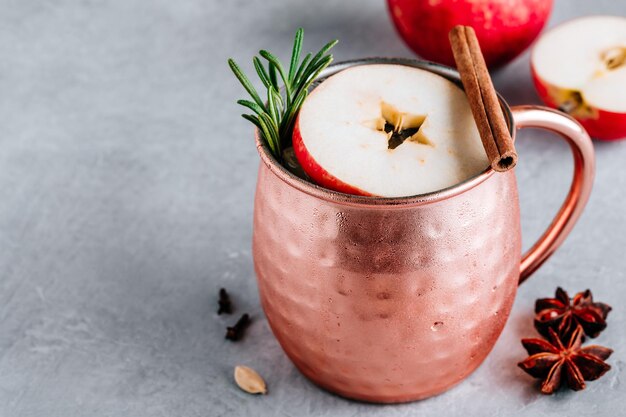 Apple Cider Moscow Mule cocktail with cinnamon stick and rosemary in copper on gray concrete stone background