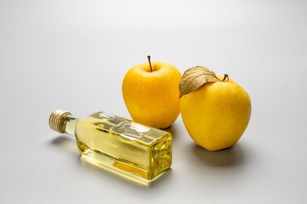 Apple cider vinegar in a glass bottle and fresh yellow apples on the gray background