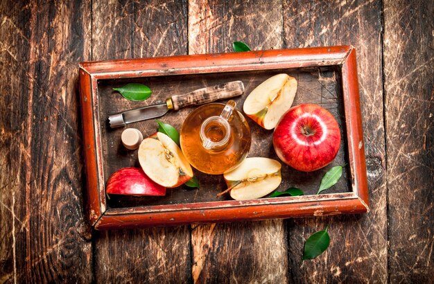 Apple cider vinegar, red apples in the old tray . On wooden table.