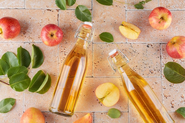 Apple cider vinegar in a two glass bottles and fresh apples with leaves on beige concrete background top view close up