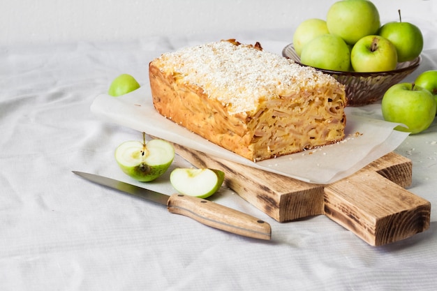 Apple and coconut oaf cake on wooden cutting board and apples in a vase