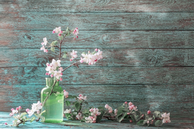 古い木製のテーブルの上の緑のガラス花瓶のリンゴの花