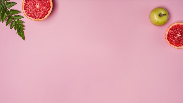 Apple, grapefruit and green leaves on the pink background