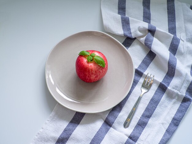 Apple and green basil on the beige plate with fork on white table