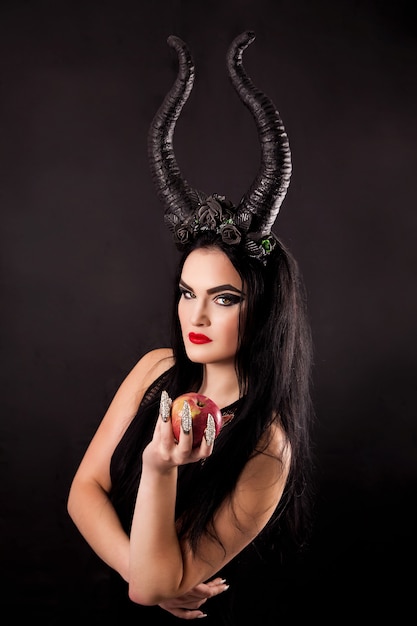 An apple in the hands of a horned witch