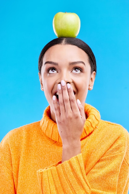 Apple head balance woman face and surprised with fruit product for weight loss benefits healthy lifestyle or body detox Organic food diet nutritionist studio and shocked person on blue background