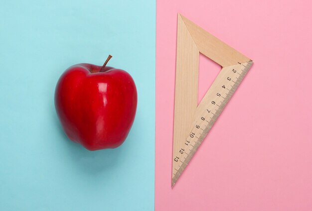 Apple, houten liniaal driehoek op roze blauw. Terug naar school. Onderwijs concept