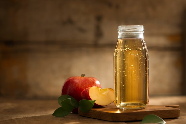 Photo apple juice in a bottle and glass with sliced red apple in wooden background