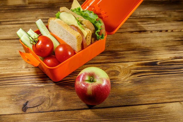 Apple and lunch box with sandwiches and fresh vegetables on a wooden table