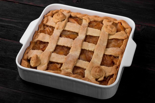 Apple pie in a square ceramic baking sheet on a dark wooden background