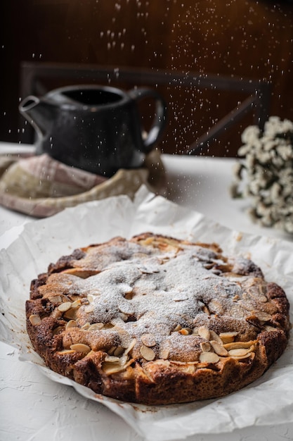 Apple pie with a tea kettle in the background and icing powder in the air