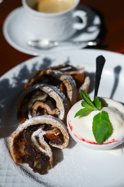 Apple strudel with melted ice cream and cup of coffee on the table in sunny day