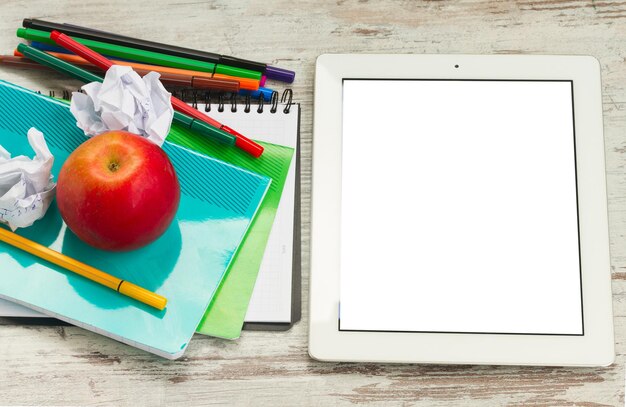 Photo apple with school supplies and tablet with empty screen on white wooden table top view