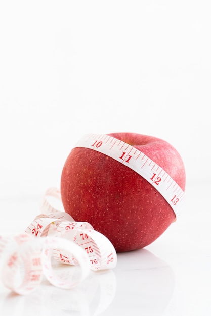 Apple wrapped with measure tape on white marble surface