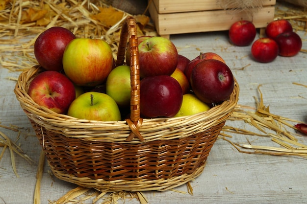 Apples in basket with straw on wooden background