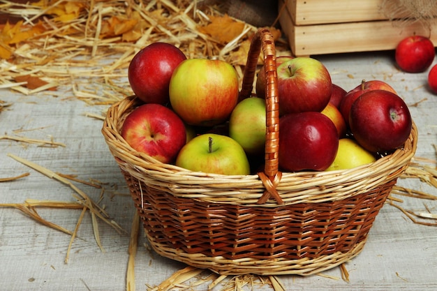 Apples in basket with straw on wooden background