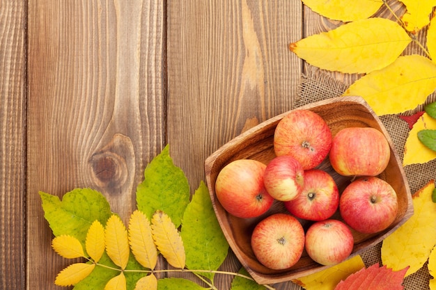 Apples in bowl and colorful autumn leaves on wooden background