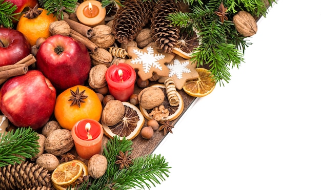 Apples, candles, tangerine fruits, walnuts, cookies and spices with christmas tree branches. Festive food background