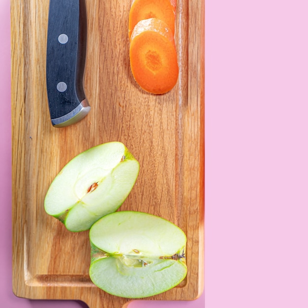 apples, carrots and knife on wooden table on pink, top view