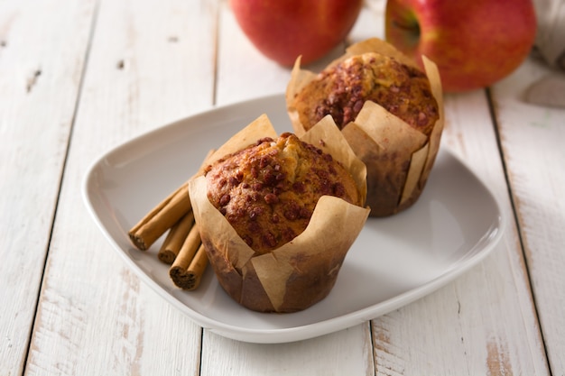 Apples and cinnamon muffins on white wooden table. 