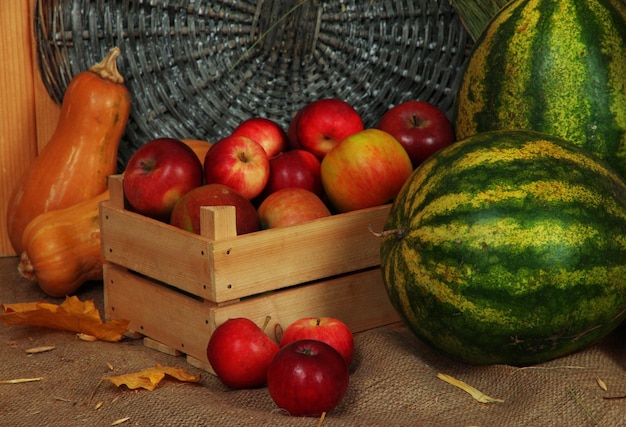 Apples in crate with watermelons and pumpkins on sackcloth on wicker background