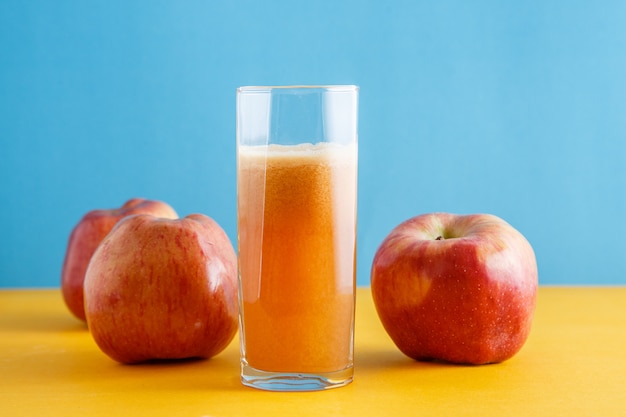 Photo apples and a glass of natural apple juice on yellow-blue background