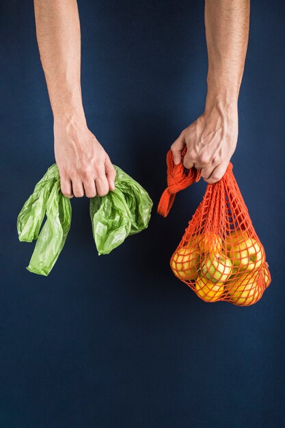 Apples and lemons in an orange string bag in one man's hand in another plastic bag