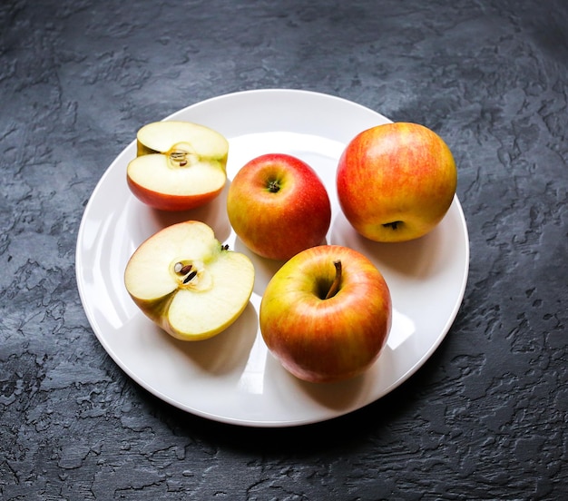 Apples lying on the white plate. Still life photo. Black background.