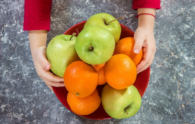 Яблоки и апельсины в руках ребенка.